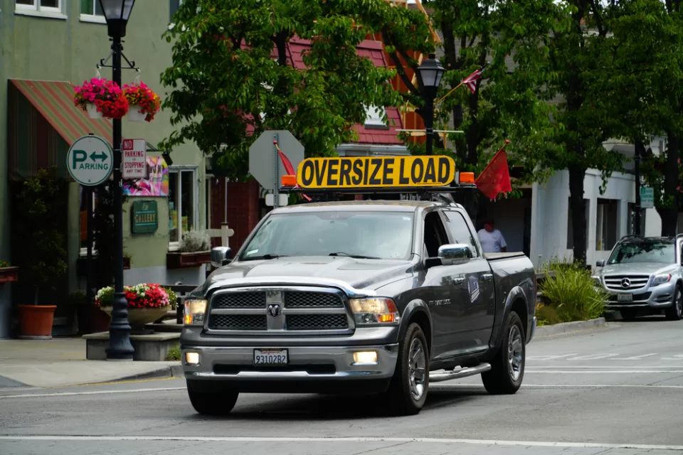 Pick-up truck on small town street with yellow "Oversize Load" sign